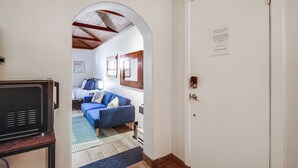 A hallway leading to a living area with a blue sofa, a wooden table, and a white door with a sign. - Cozy Beach Studio – Sleeps 2, Walk to Ocean (San Diego)