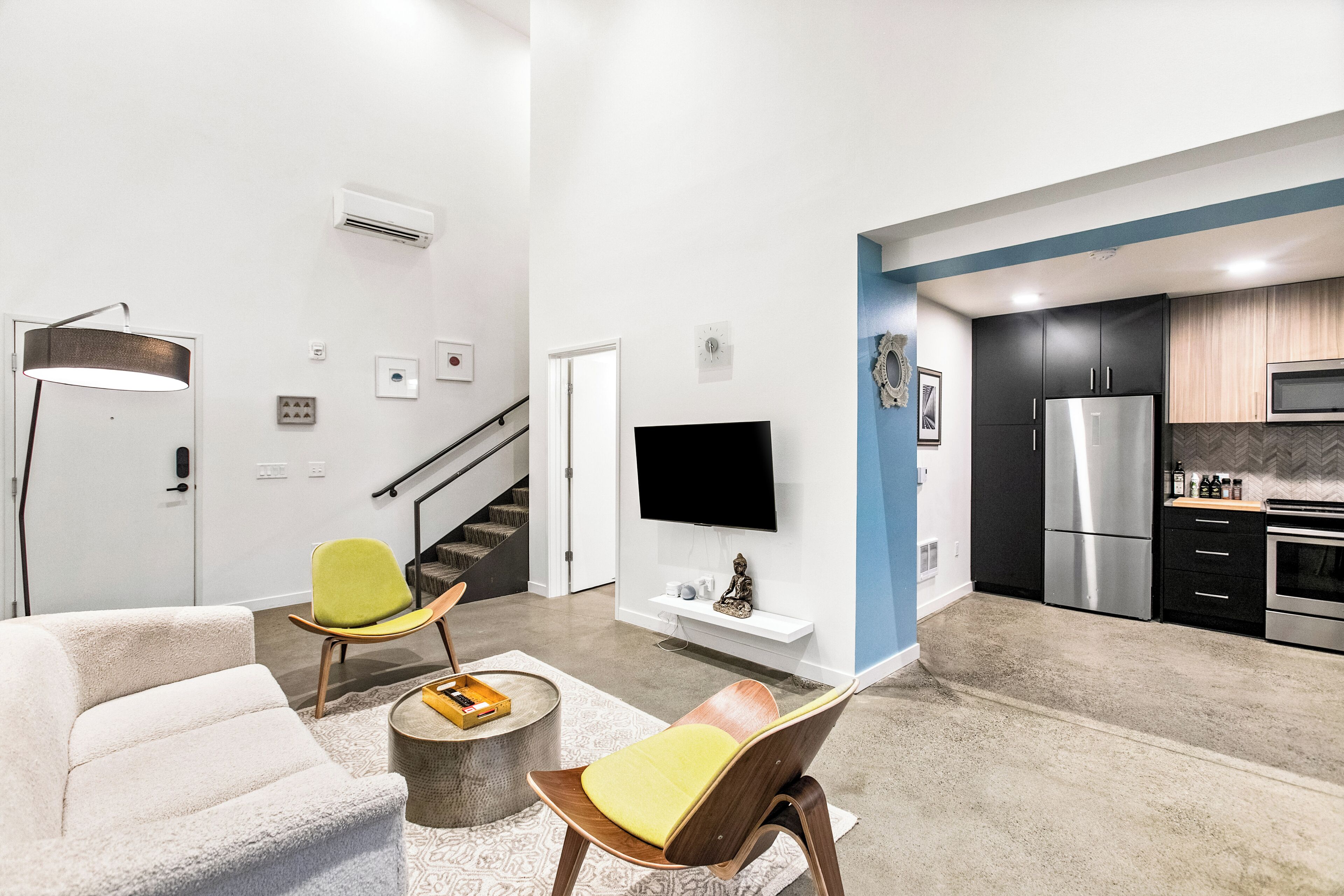 Una sala de estar moderna con un sofá, dos sillones, una mesa de centro y un televisor de pantalla plana montado en la pared.