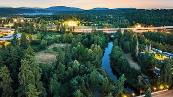 An aerial view of a forested area with a river, a bridge, and buildings with lights.