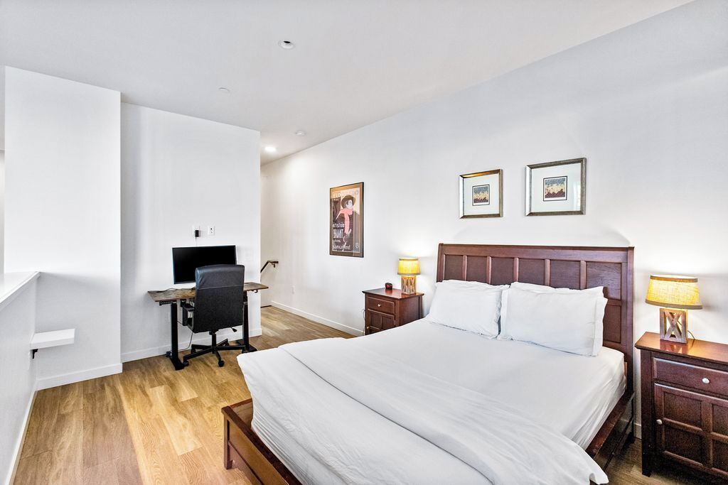 A hotel room with a large bed, a desk with a computer, and two bedside tables with lamps.