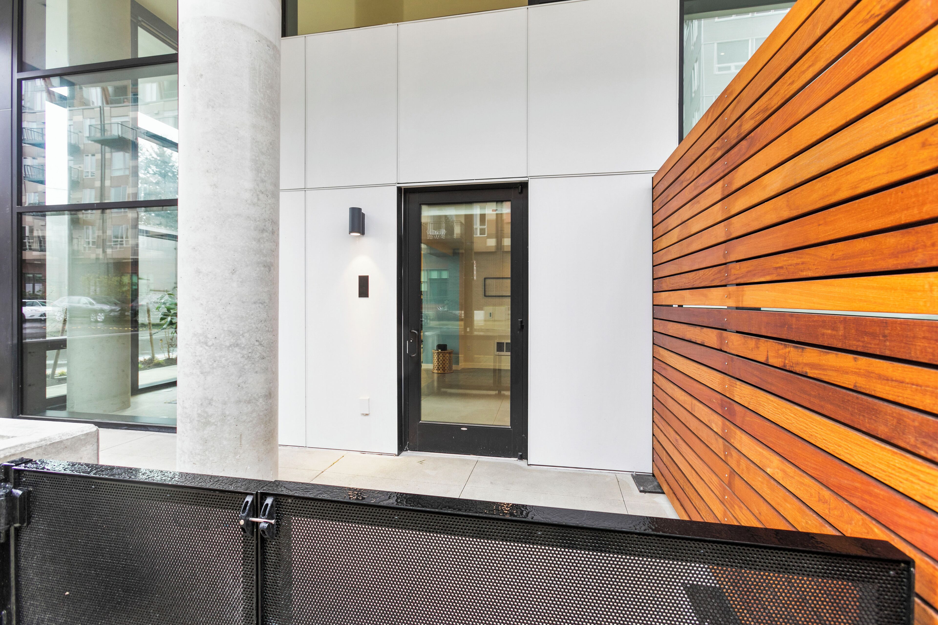 A modern building exterior with a glass door, a wooden slatted wall, and a metal fence.
