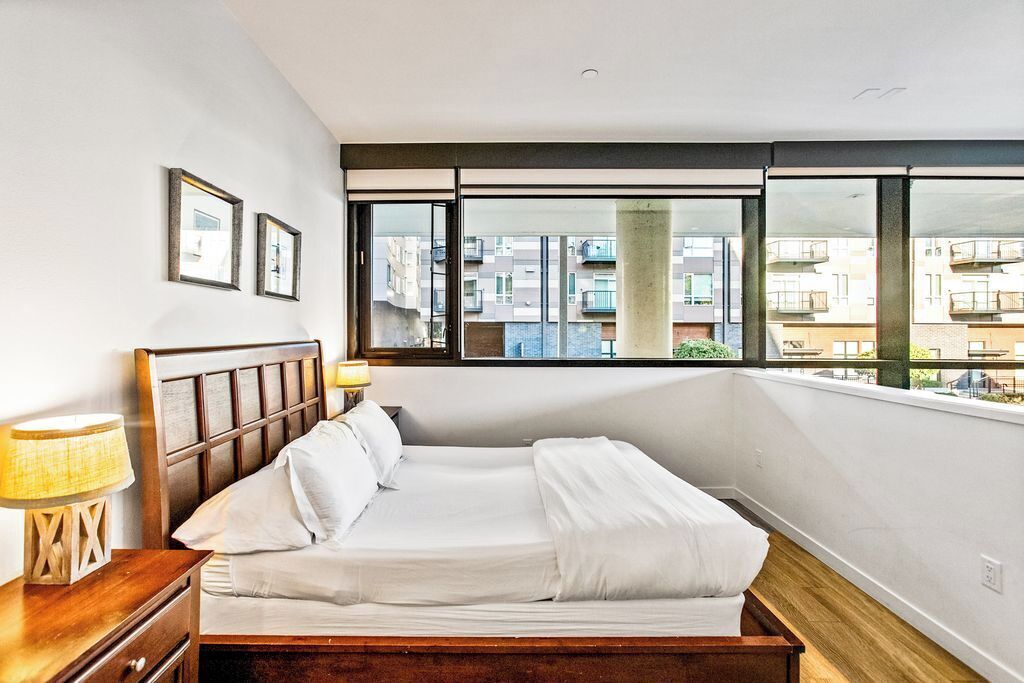 Une chambre à coucher avec un grand lit, une table de chevet et une fenêtre donnant sur des immeubles.