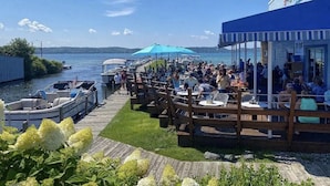 A waterfront restaurant with outdoor seating, boats docked nearby, and a view of the water. - Torch Lake Sandbar Escape (Rapid City)