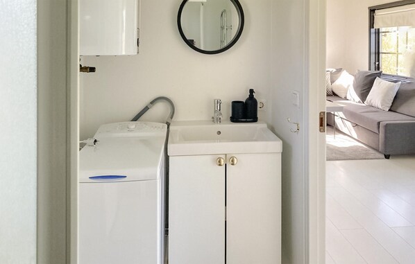 Ein kleines Badezimmer mit Waschmaschine, Waschbecken und Spiegel.