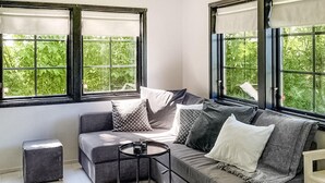 A modern living room with a grey sofa, multiple cushions, a small round table, and large windows offering a view of greenery. - Gorgeous home in Skivarp with kitchen (Skivarp)