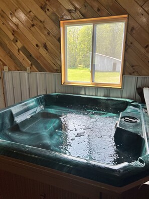 Ein Whirlpool in einer Holzhütte mit Blick auf einen Garten.
