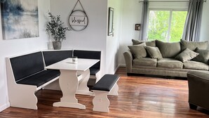 Ett modernt vardagsrum med ett vitt matbord, en svart, vadderad bänk och en beige soffa.