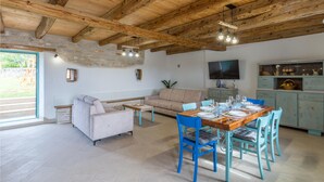A rustic interior with exposed wooden beams, a stone wall, a sofa, a dining table set for six, and a television on the wall. - Beautiful home in Buje (Buje)