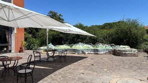 Ein Außenbereich mit einer Terrasse, Steinböden, weißen Sonnenschirmen und Metallstühlen.