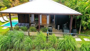 Ein modernes Haus mit überdachter Terrasse, Swimmingpool und üppiger Bepflanzung.