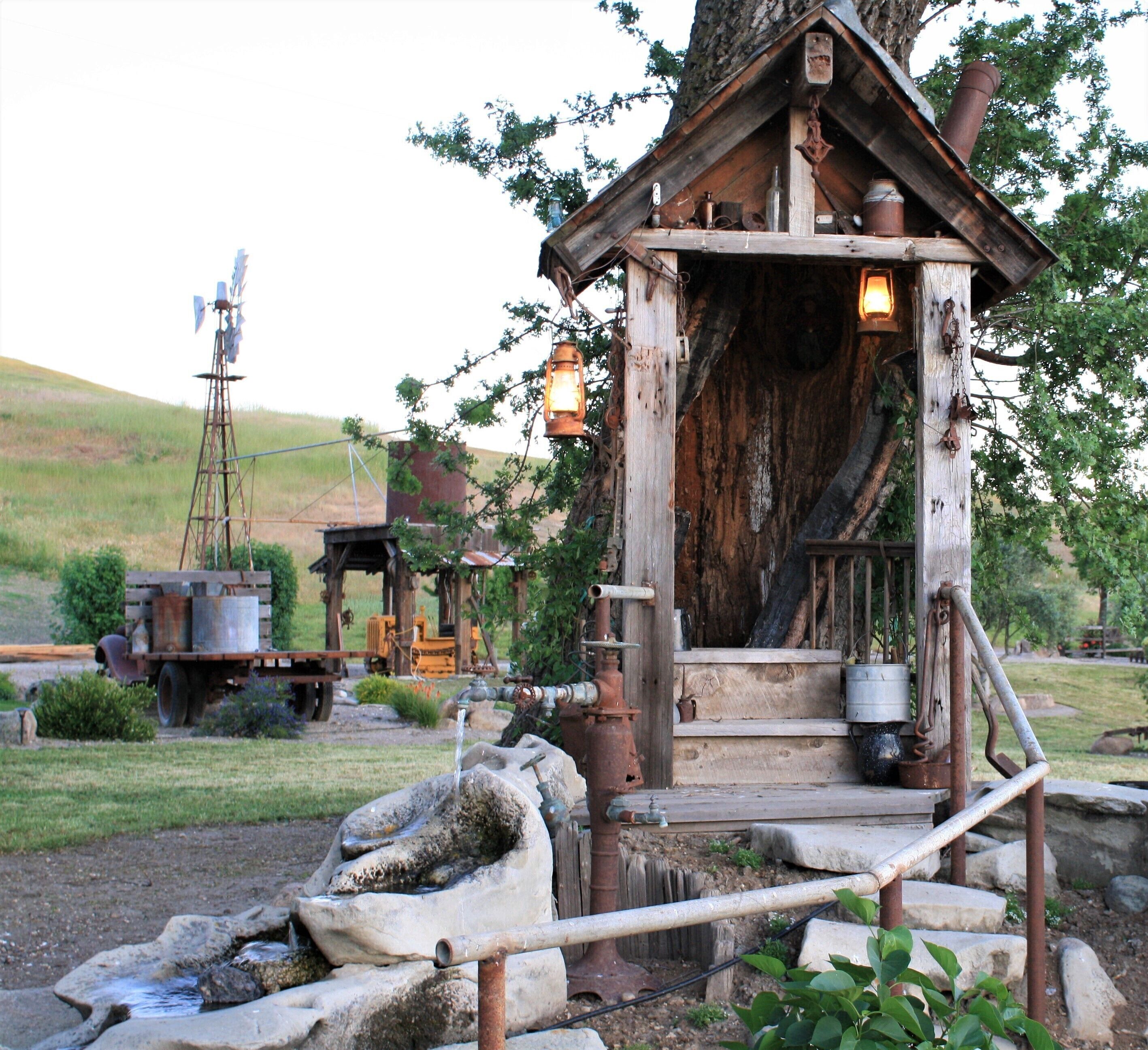 Une cabane en bois rustique, avec un puits en pierre et un moulin à vent en arrière-plan.