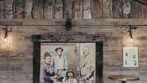 A pool table with a red felt surface, a white cue ball, and a set of pool balls. There is a wooden ceiling with exposed beams and a rustic wall with a framed painting. A small round table with a black base is visible to the right. - Paso Robles Ultimate Farm Stay! Country Oasis!! Very Unique!!! (San Miguel)