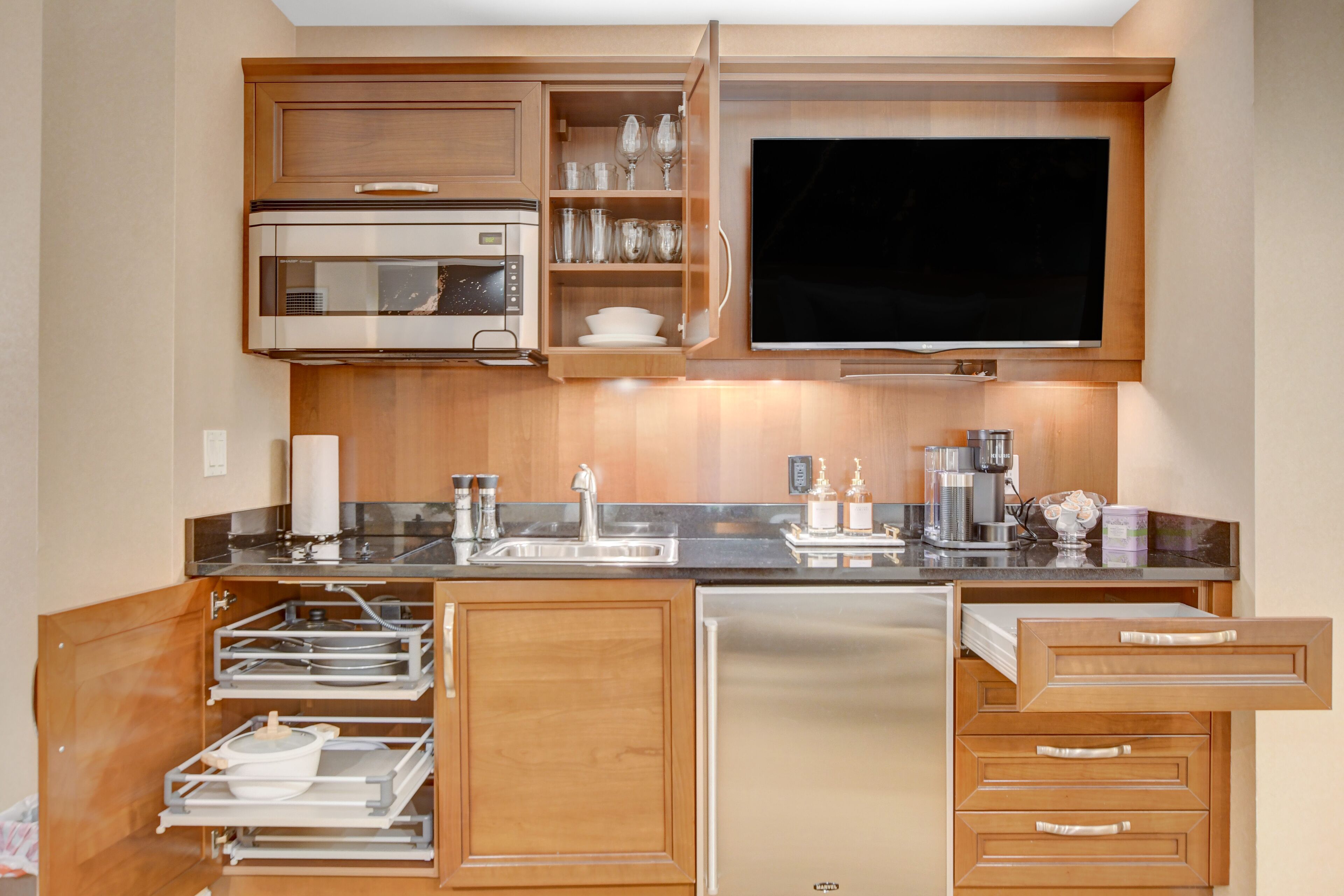 A modern kitchen with wooden cabinets, a built-in oven, a refrigerator, and a flat-screen TV.