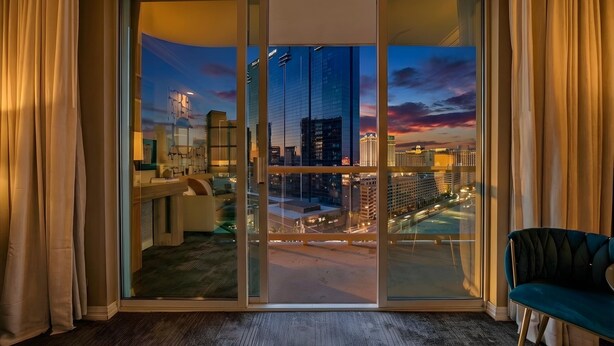 A hotel room with a large sliding glass door leading to a city view at dusk. - The Suite Spot@MGM Signature Balcony Strip View (Las Vegas)