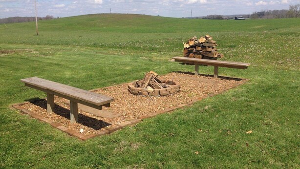 Un espace pique-nique équipé d’un foyer, de bancs et d’un terrain herbeux.