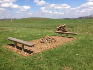 A picnic area with a fire pit, benches, and a grassy field. - Country setting with mature trees, large deck. Game/Rec room, Fire Pit and Grill (Austin)