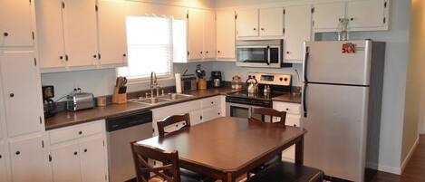 A compact kitchen with white cabinets, a microwave, a refrigerator, and a dining table with chairs.