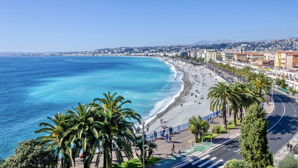 Un paisaje urbano costero con playa, palmeras y una calle con peatones.