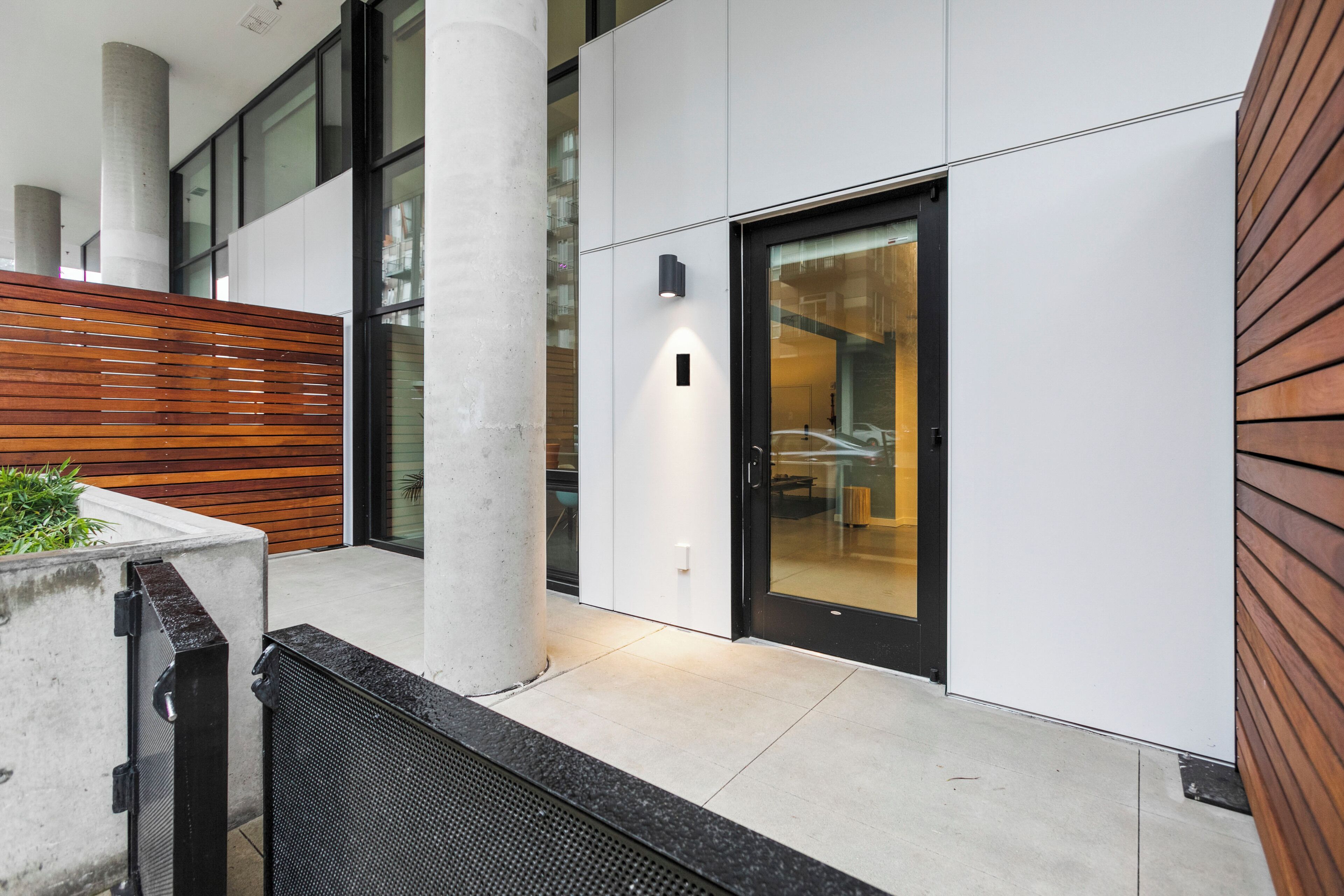 A modern building exterior with a glass door, concrete pillars, and a wooden slatted wall.