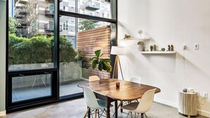 A modern dining area with a large window, a wooden table, and white chairs. - Open Loft in Redmond Core - 92 Walkscore (Redmond)