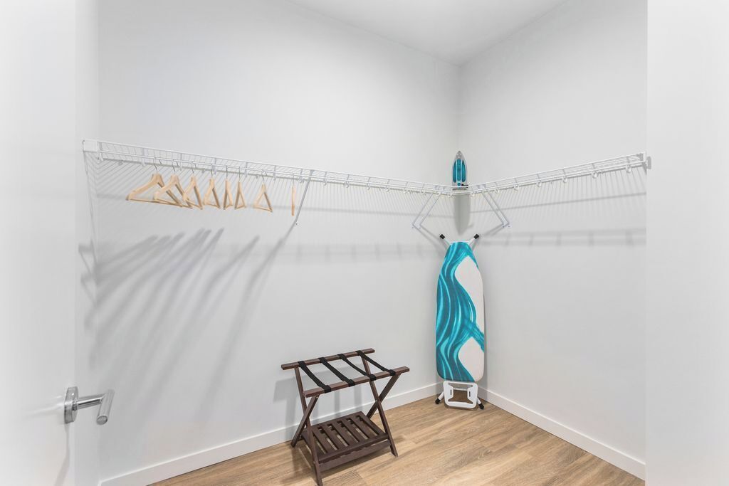 A laundry area with a drying rack, a hanging clothes rack, and a blue ironing board.