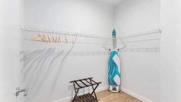 A laundry area with a drying rack, a hanging clothes rack, and a blue ironing board.