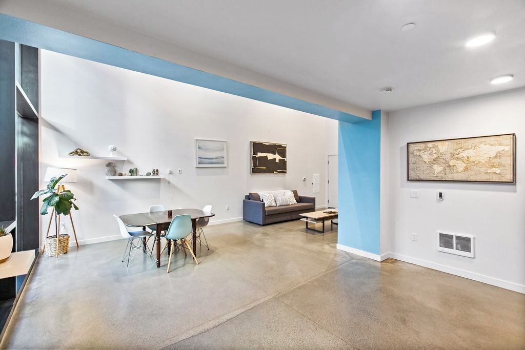 Ampla sala de estar com mesa de jantar, sofá e uma grande pintura abstrata na parede.