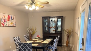 A dining area with a long table, patterned chairs, a ceiling fan, and a cabinet with glass doors. - South County ranch house walking distance to Grant Trail (St. Louis)
