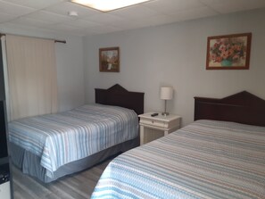 A hotel room with two single beds, a nightstand with a lamp, and two framed pictures on the wall. - Hickory Shades Motel (Nashville)