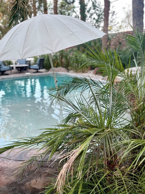 A pool area with a white umbrella, palm trees, and lounge chairs.