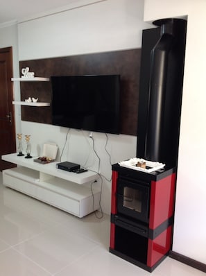 Uma sala de estar moderna com uma televisão de tela plana presa a uma parede escura, um móvel branco embaixo e uma lareira a lenha preta e vermelha.