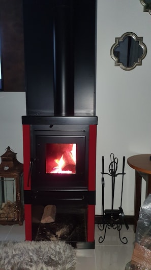 Uma lareira a lenha com moldura vermelha, um suporte de metal com velas e um espelho decorativo na parede.