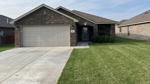 A residential house with a garage, a well-maintained lawn, and a brick exterior. - 1-800 We got the stay (Amarillo)