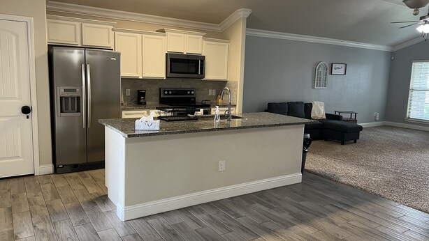 A modern kitchen with a central island, stainless steel appliances, and a dark wood floor. - 1-800 We got the stay (Amarillo)