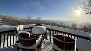 Un muelle cubierto de nieve con sillas Adirondack y vistas a un paisaje nevado y montañas distantes.