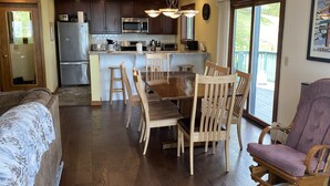 Una cocina amplia con armarios de madera oscura, un refrigerador de acero inoxidable y un microondas. Hay una zona de comedor con una mesa y sillas de madera, y un ventanal que ofrece vistas al exterior.