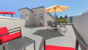A rooftop patio with a table and chairs, a red sofa, and a beige umbrella. - Golden Gardens Getaway Beach Waterfront (Seattle)