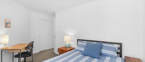 Un dormitorio con una cama, un escritorio, una silla, una mesita de noche y una lámpara.