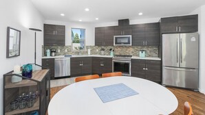 A modern kitchen with dark cabinetry, stainless steel appliances, and a round dining table. - Golden Gardens Getaway Beach Waterfront (Seattle)