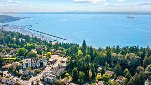 An aerial view of a coastal town with residential buildings, a marina, and a large body of water. - Golden Gardens Getaway Beach Waterfront (Seattle)