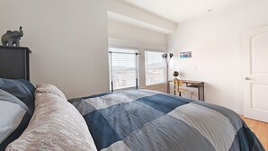 A bedroom with a bed, a desk, and a chair. There is a window with blinds, a door, and a small statue on a nightstand. - 9 - Peaceful & Spacious 4B2B Upper Unit near FW (Daly City)