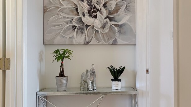A hallway with a white door, a grey floral painting, a metal console table with a potted plant, a decorative elephant figurine, and a small potted plant. - 9 - Peaceful & Spacious 4B2B Upper Unit near FW (Daly City)