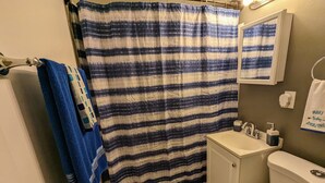 Un baño con cortina de ducha a rayas, un lavabo, un inodoro y un perchero con una toalla azul.
