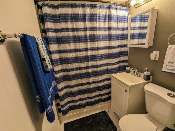 Un baño con cortina de ducha a rayas, un lavamanos, un inodoro y un perchero para toallas.