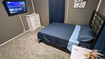 A bedroom with a bed, a TV, a desk, and a wall-mounted artwork.