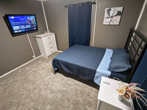 Un dormitorio con cama, televisor, escritorio y una obra de arte en la pared.