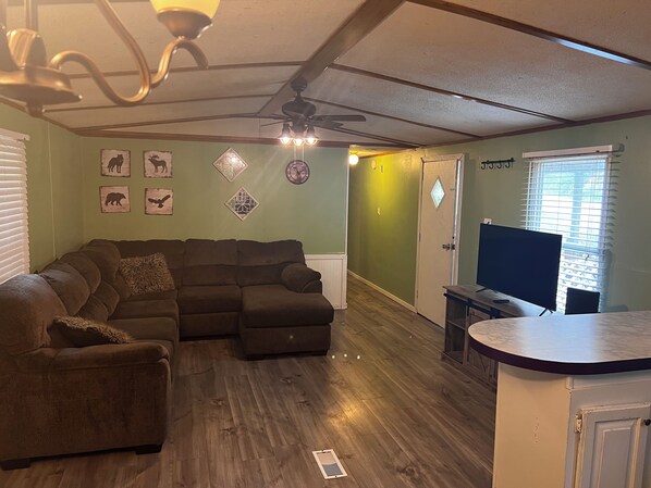 A living room with a sectional sofa, a ceiling fan, and a flat-screen TV.