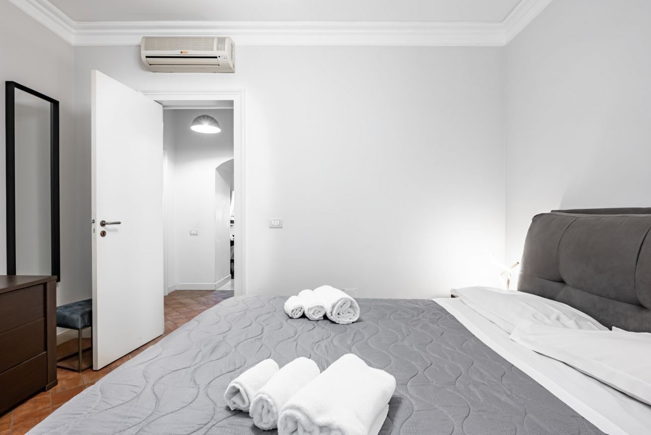 A hotel room with a bed, a dresser, a door leading to another room, and an air conditioning unit.
