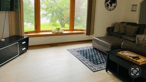 Un salon avec une grande fenêtre, un canapé noir, une table basse et un meuble pour la télévision.
