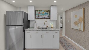 A modern kitchen with white cabinetry, a stainless steel refrigerator, a granite countertop, and a sink with a gold faucet. - Seaside Heights' Palm Tree Paradise: 3BR (Seaside Heights)